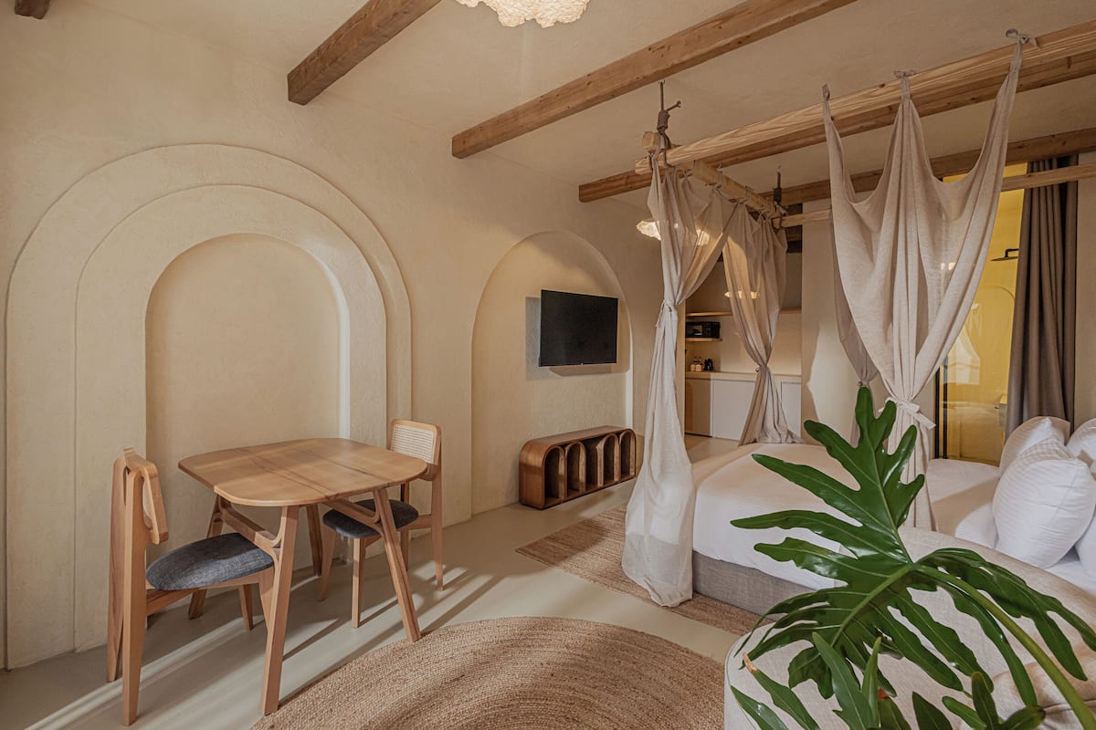A room with a wooden dining table and chairs, a sofa with a canopy, and a large plant.