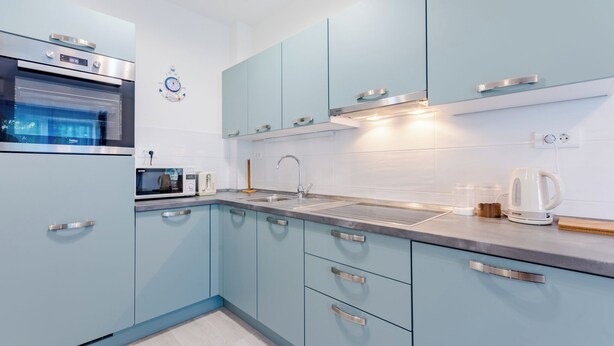 A modern kitchen with light blue cabinets, stainless steel appliances, and a built-in oven. - Apartment Karlo (Kastela)