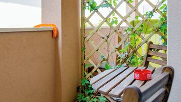 A wooden bench with a cushion, a potted plant, and a red container on a balcony.