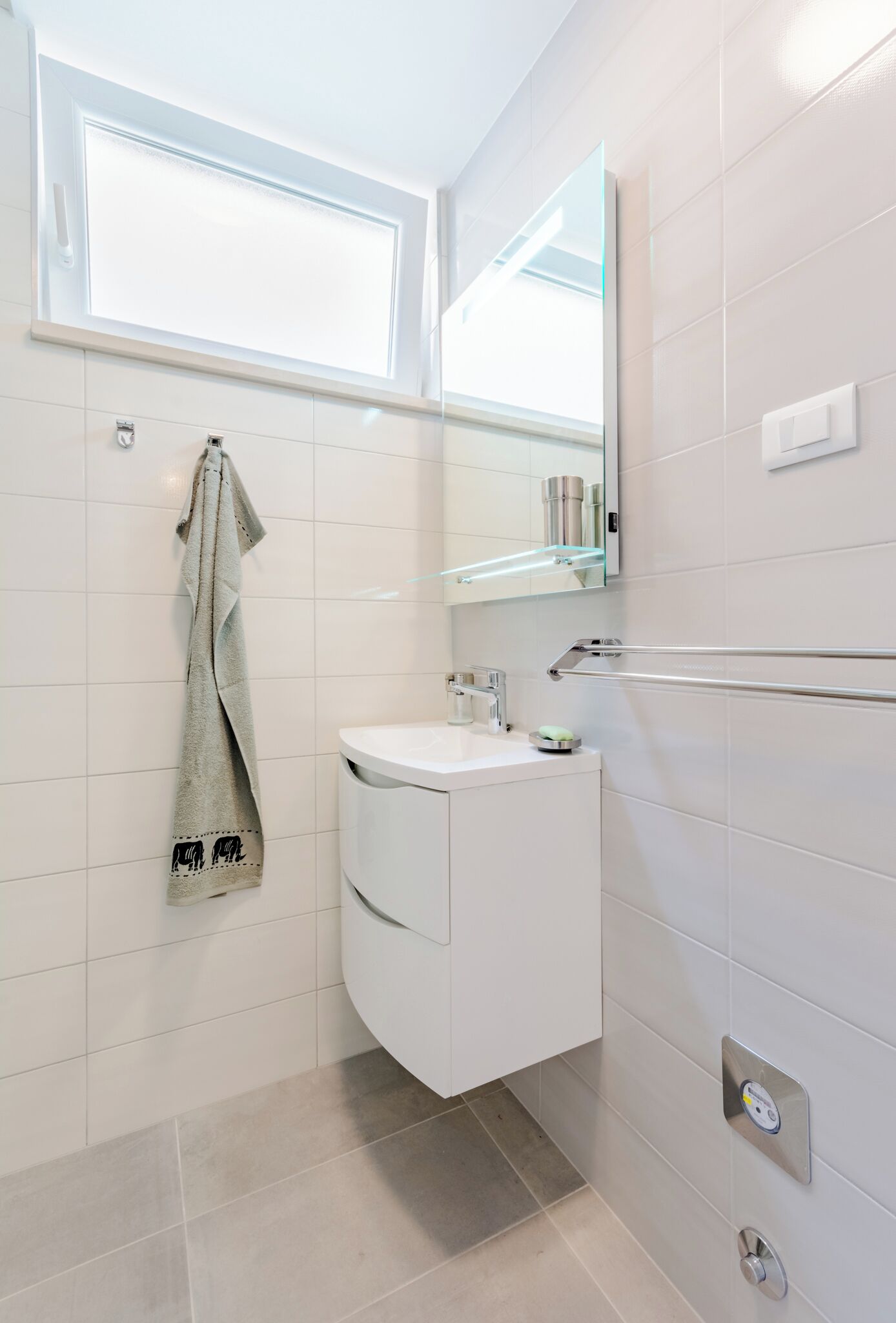 A modern bathroom with a white vanity, a towel hanging on the wall, a glass shower enclosure, and a mirror above the sink.