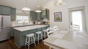 A modern kitchen with a central island, bar stools, and a dining table.