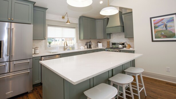 A modern kitchen with a large island, stainless steel appliances, and light green cabinetry.
