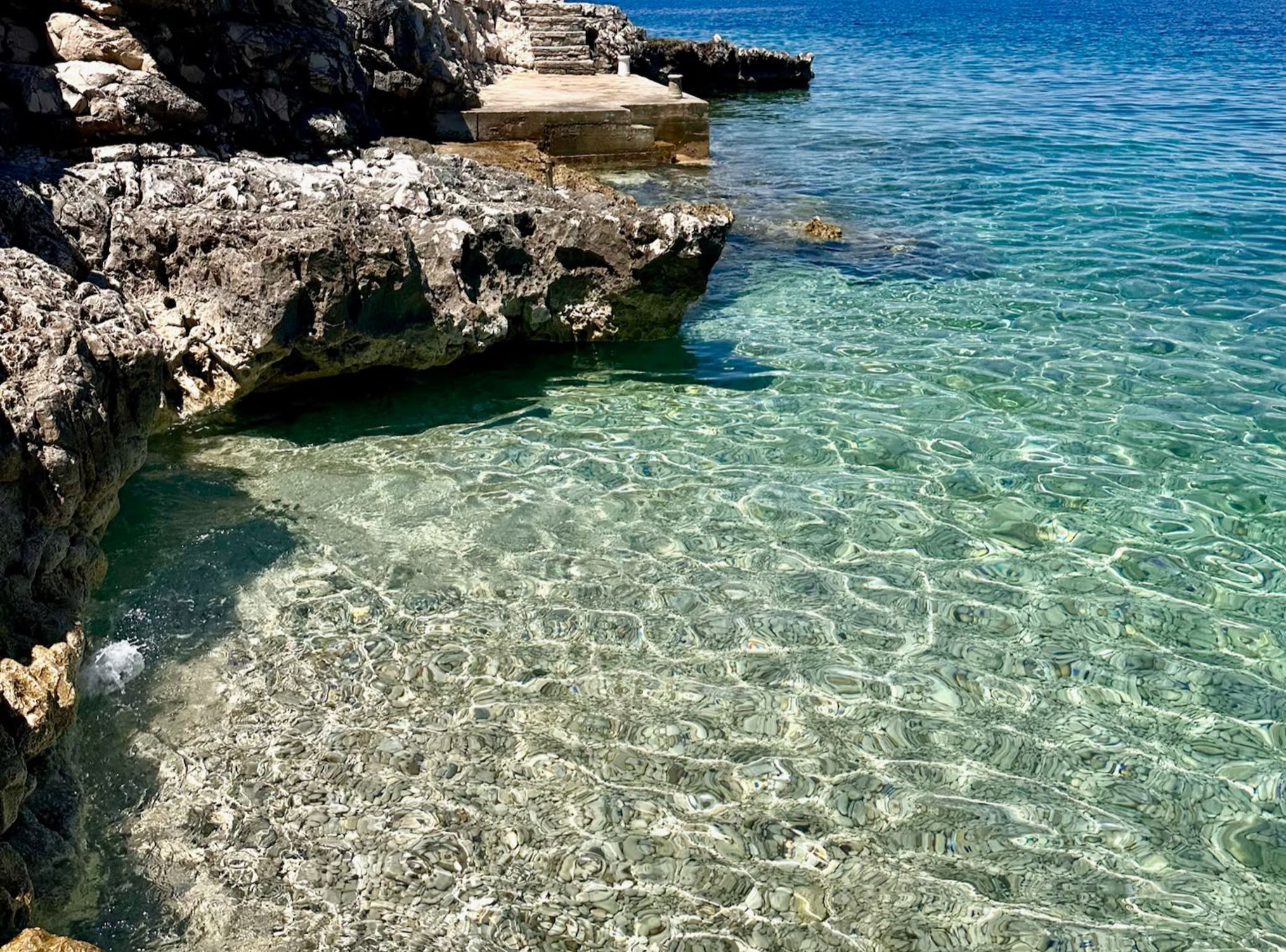 A rocky coastline with clear water, a concrete platform, and a staircase leading up.