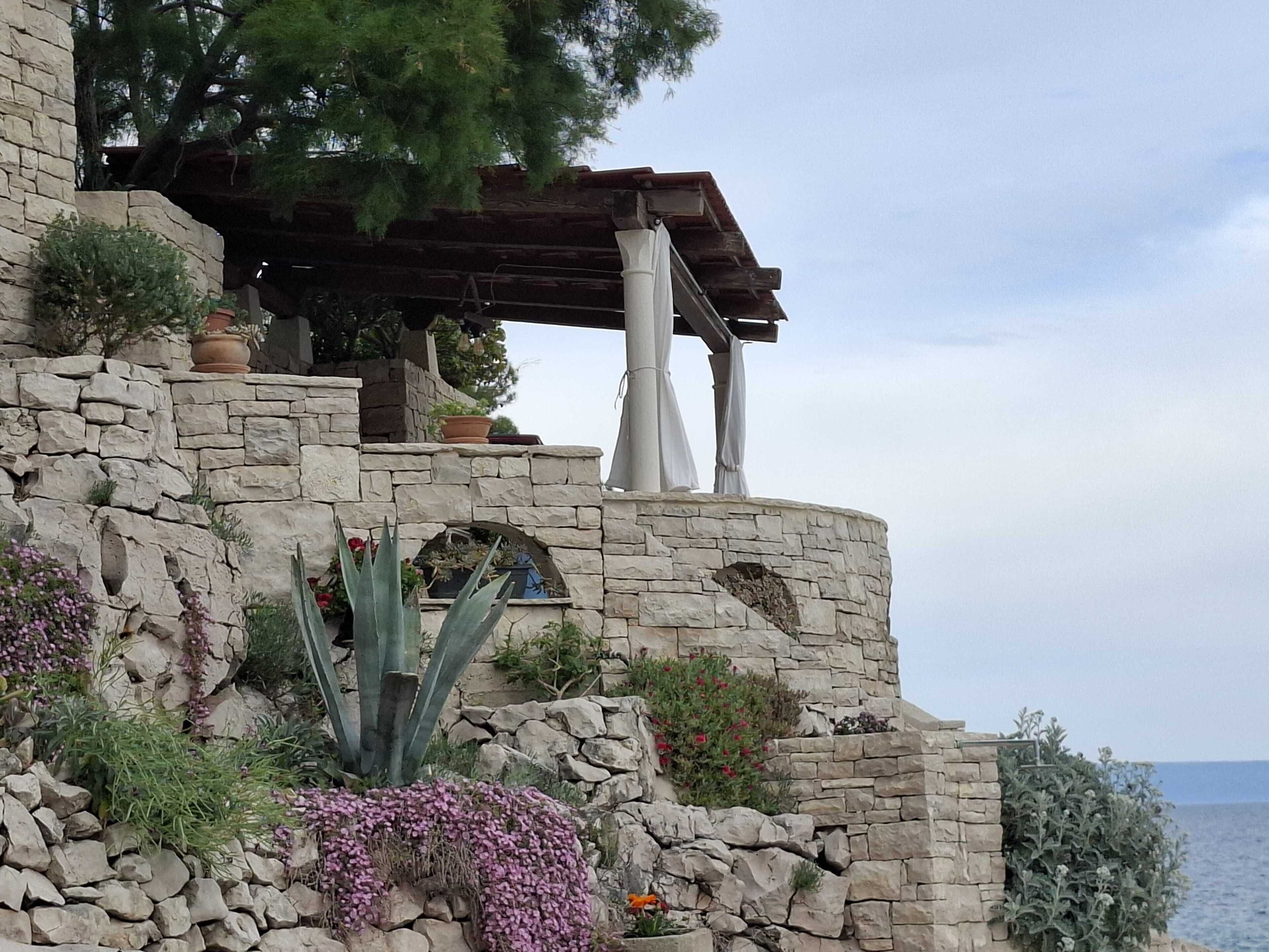 A stone building with a wooden pergola and potted plants.