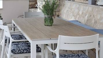 Un área de comedor al aire libre con pared de piedra, plantas en macetas y una mesa de madera.