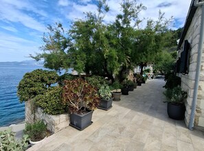 A paved outdoor area with potted plants, a stone wall, and a view of the sea. - Holiday Home Luna (Korcula)
