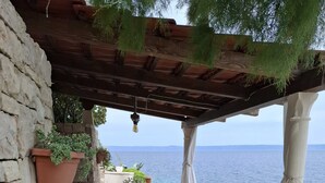 A stone wall, a wooden table with chairs, potted plants, and a view of the sea. - Holiday Home Luna (Korcula)
