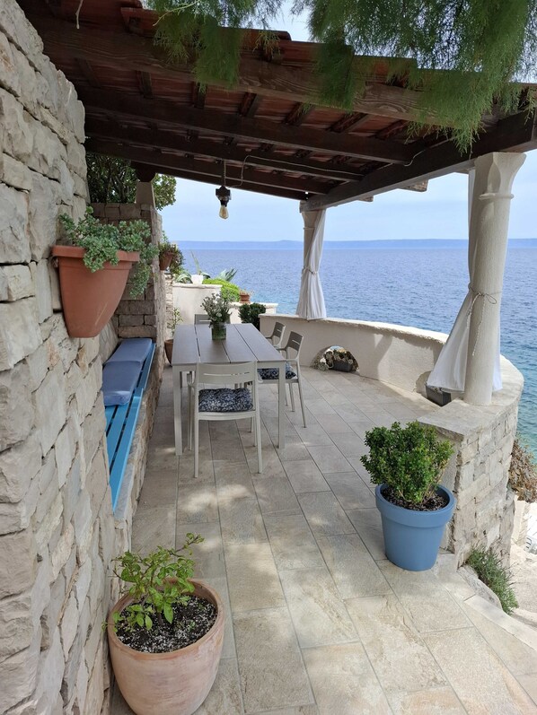 A stone wall, a wooden table with chairs, potted plants, and a view of the sea. - Holiday Home Luna (Korcula)