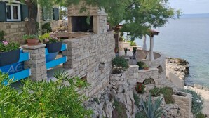 A stone-built outdoor area with a view of the sea, featuring a stone bench, potted plants, and a pergola. - Holiday Home Luna (Korcula)