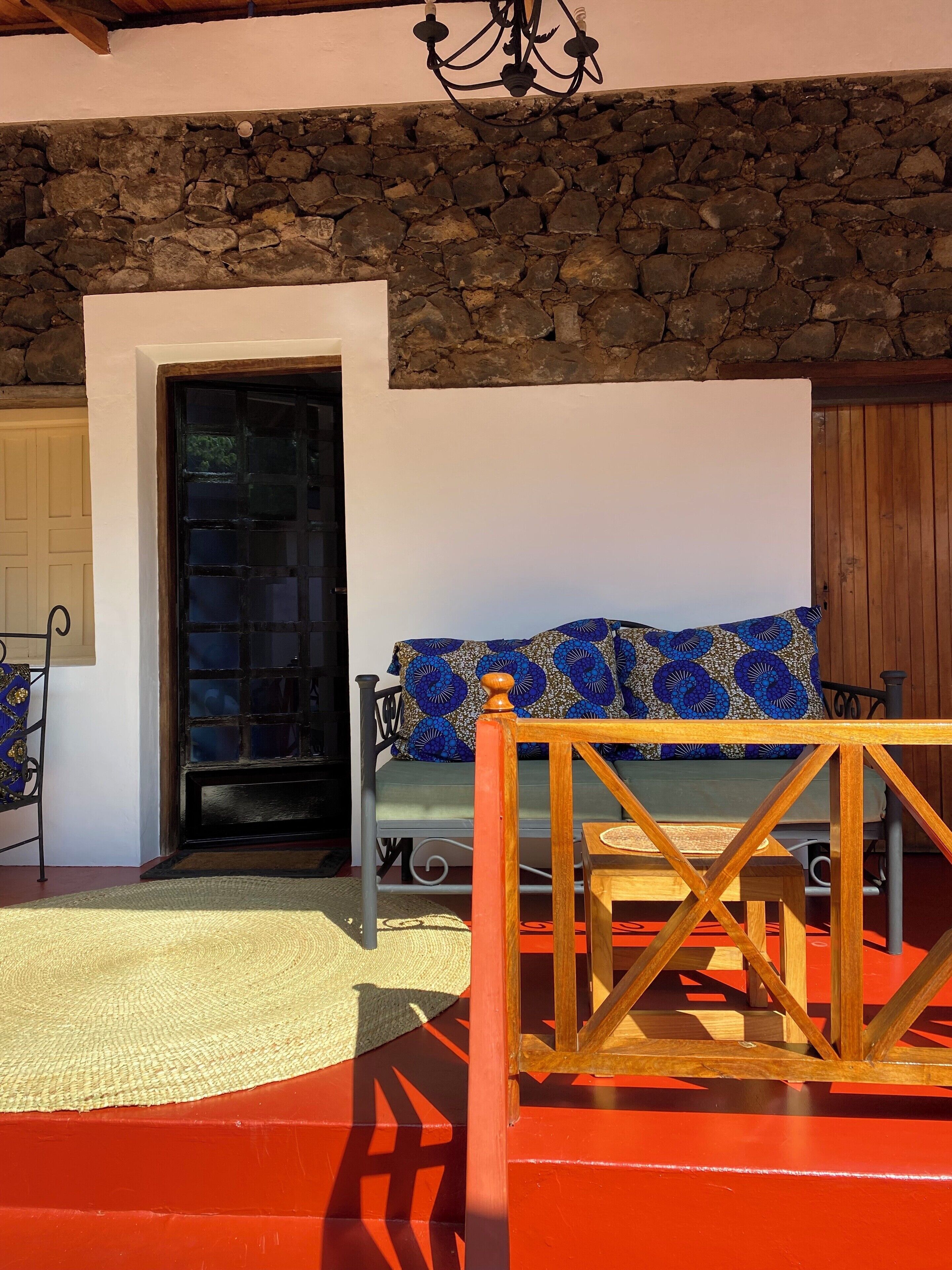 A cozy room with a stone wall, a wooden bench, a patterned cushion, and a wooden railing.