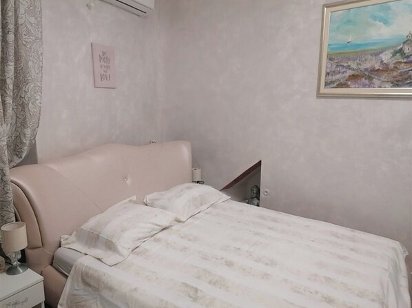 A bedroom with a bed, a nightstand, a lamp, a painting on the wall, and a decorative item on the nightstand.