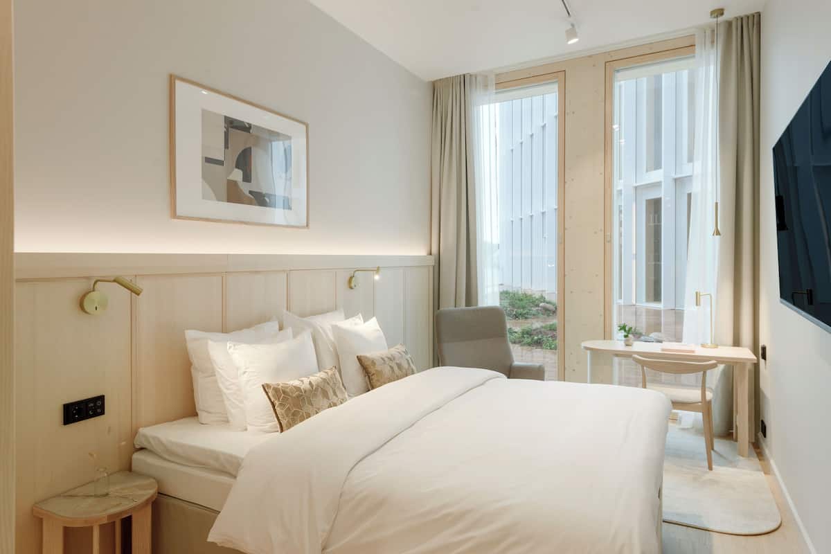 A modern hotel room with a large bed, a desk, and a view of the outdoors.