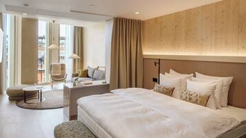 A modern hotel room with a large bed, a round coffee table, a chair, and a view of the city.