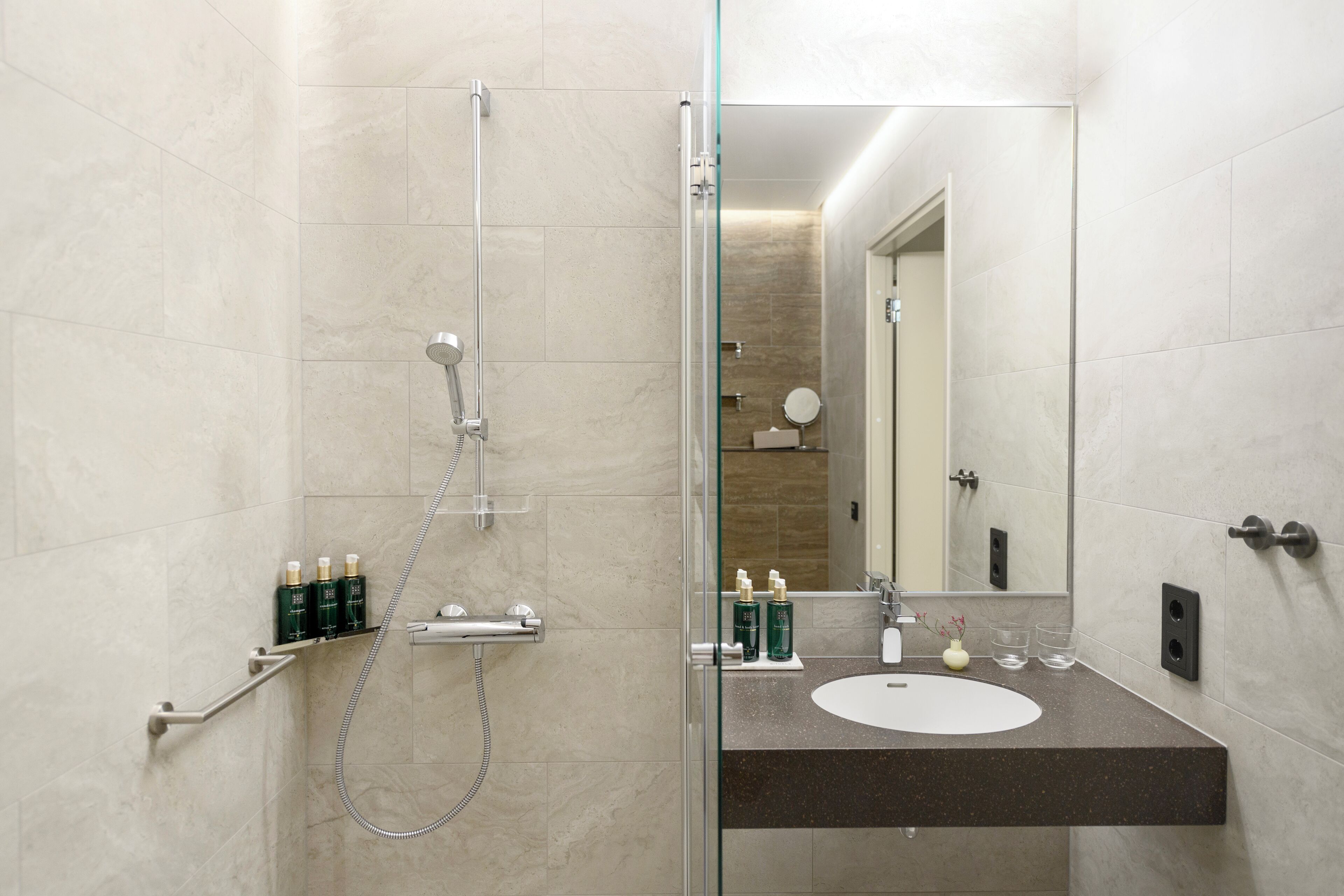 A modern bathroom with a glass-enclosed shower, a sink with toiletries, and a mirror.