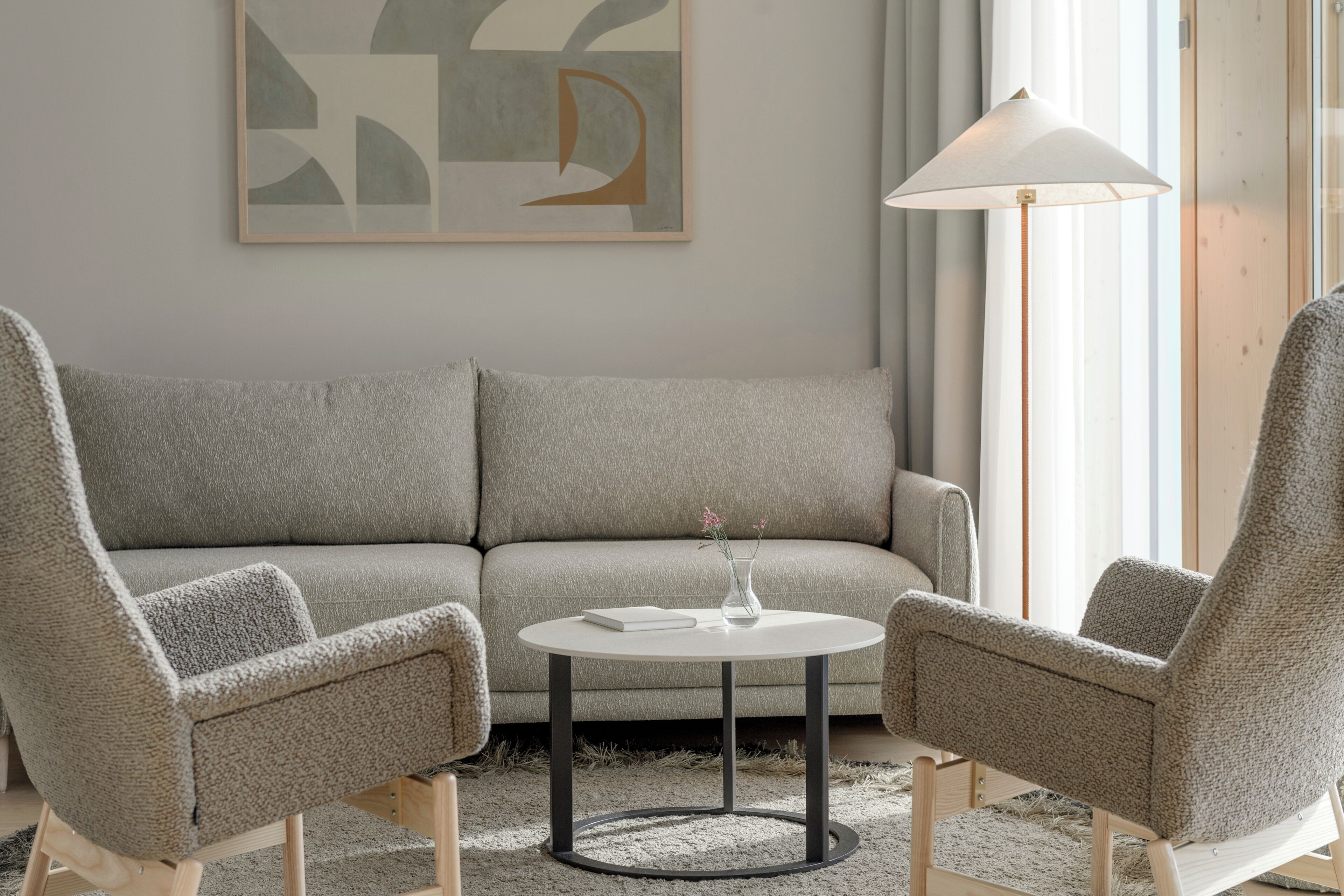 Una sala de estar moderna con un sofá gris, dos sillones, una mesita redonda y una lámpara de pie.