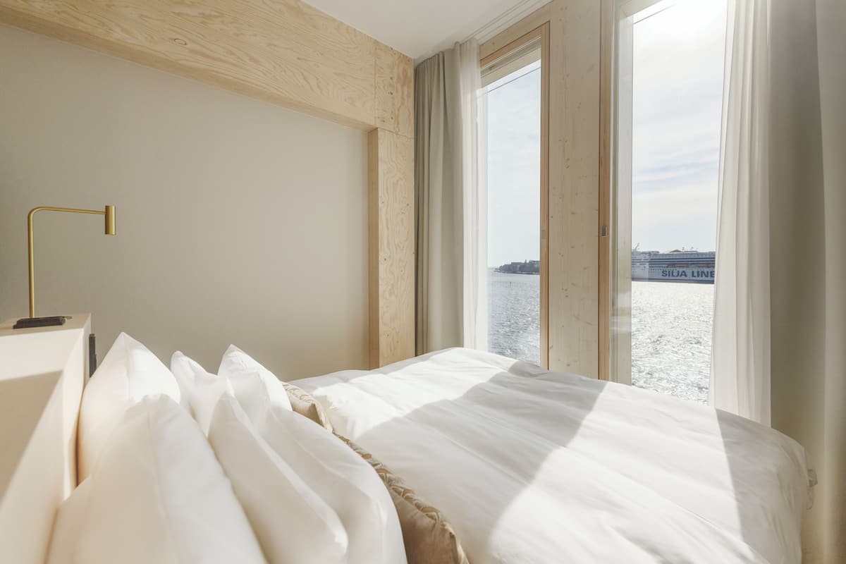 A hotel room with a bed, a bedside table, and a view of a body of water through large windows.