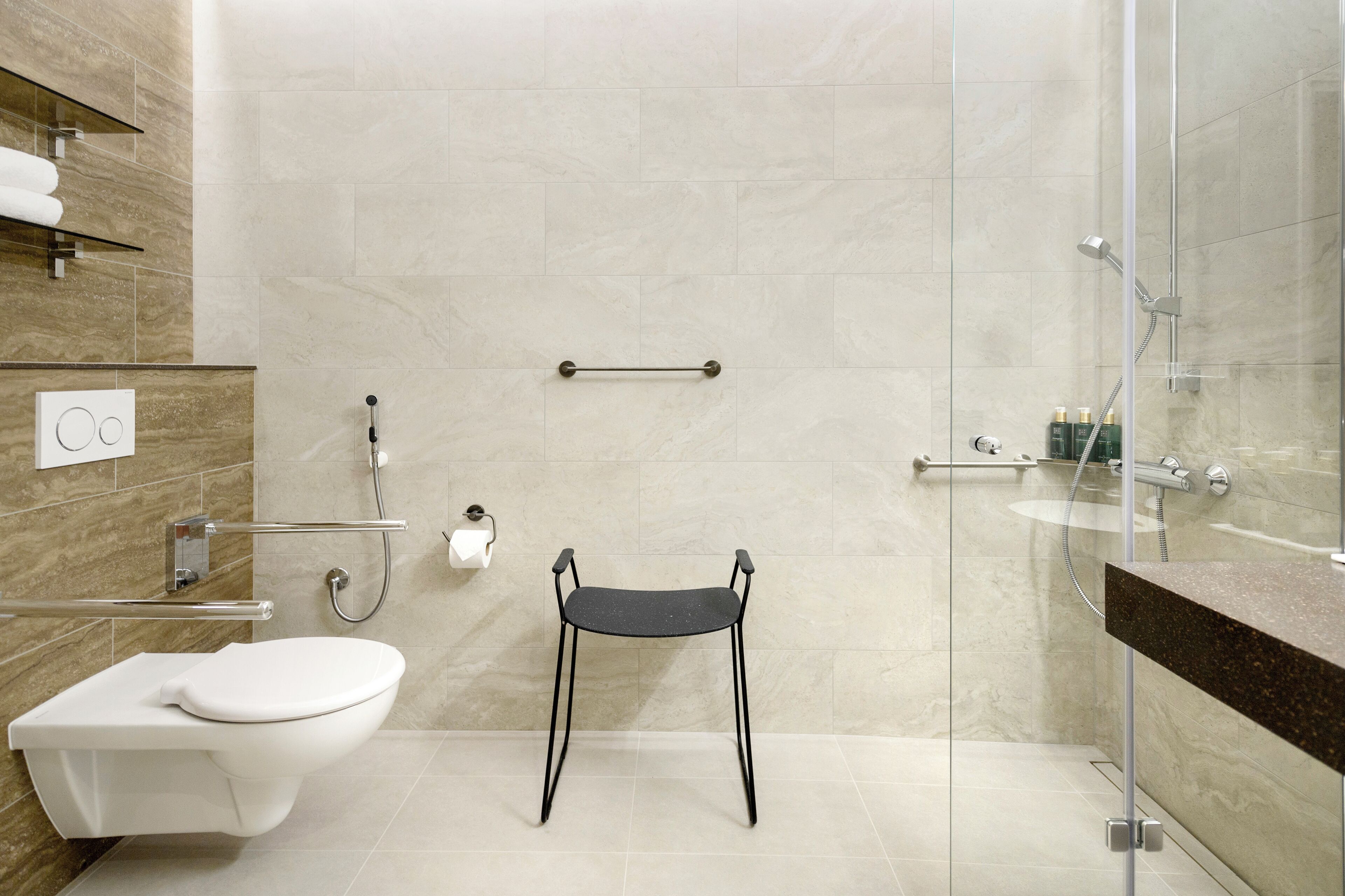 Et moderne badeværelse med toilet, en sort stol, brusekabine i glas og væg med marmorfliser.