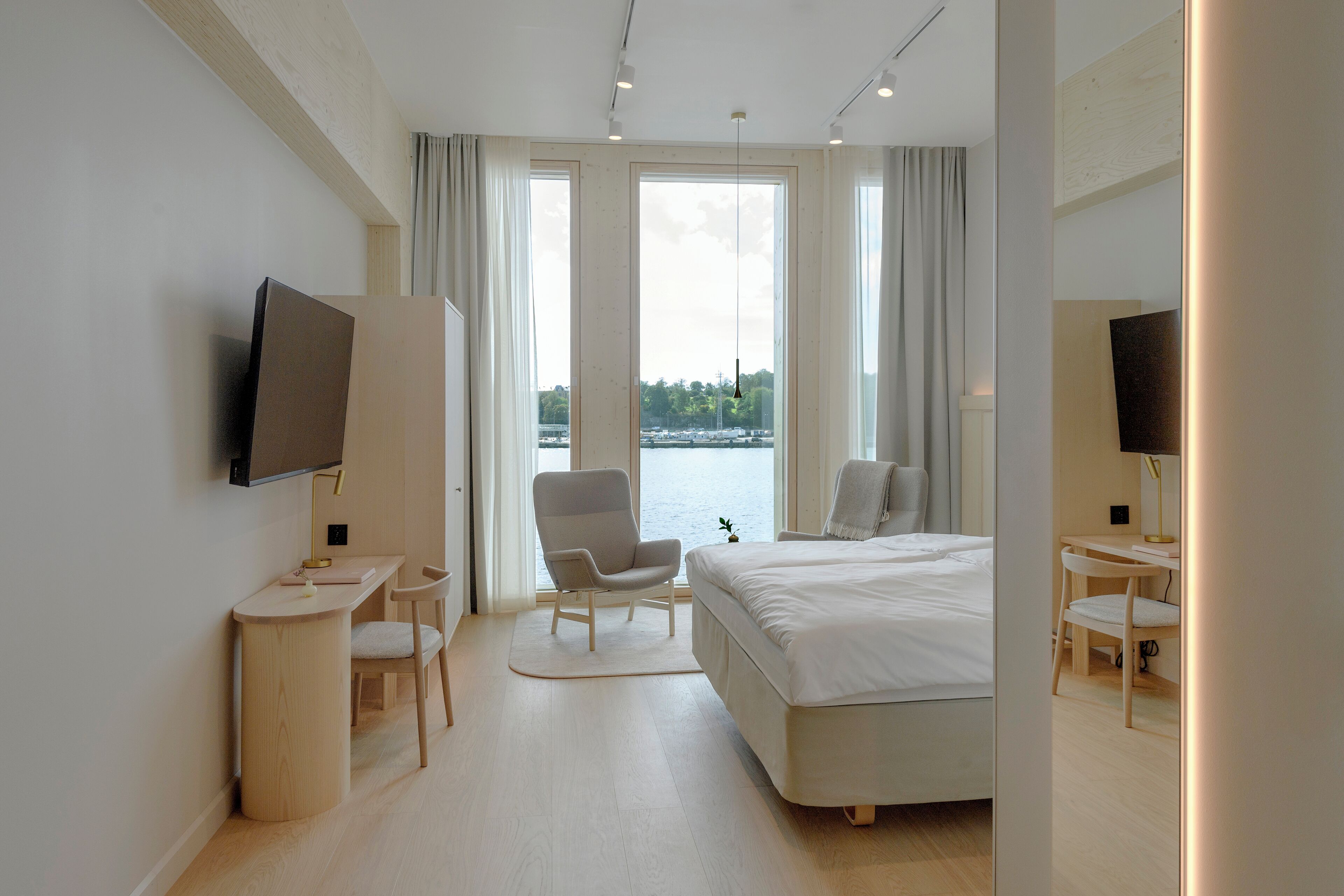 A modern hotel room with a large bed, a desk, a chair, and a TV.