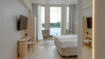 A modern hotel room with a large bed, a desk, a chair, and a TV.