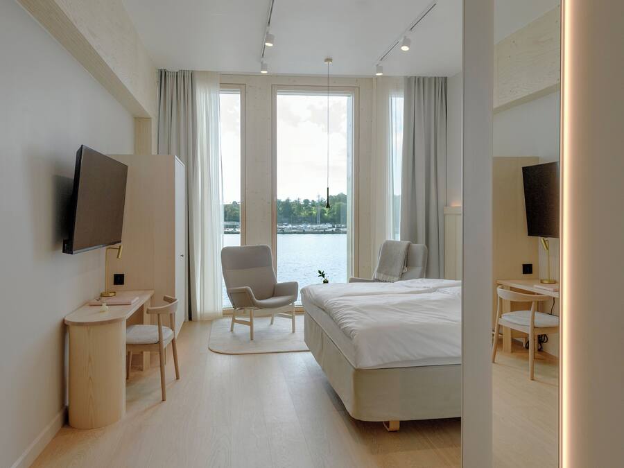 A modern hotel room with a large bed, a desk, a chair, and a TV.