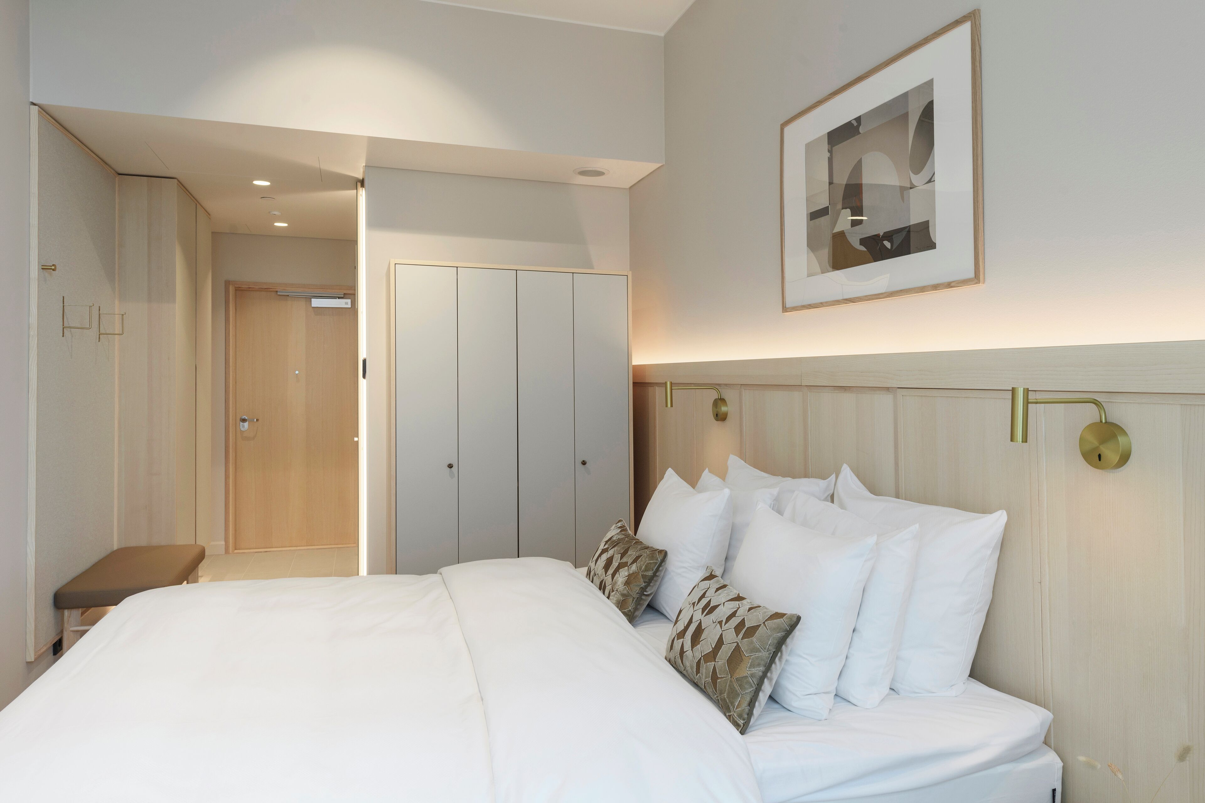 A hotel room with a large bed, a bench, a wardrobe, and a framed picture on the wall.