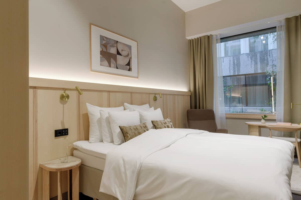 A hotel room with a large bed, bedside table, chair, and a window with curtains.