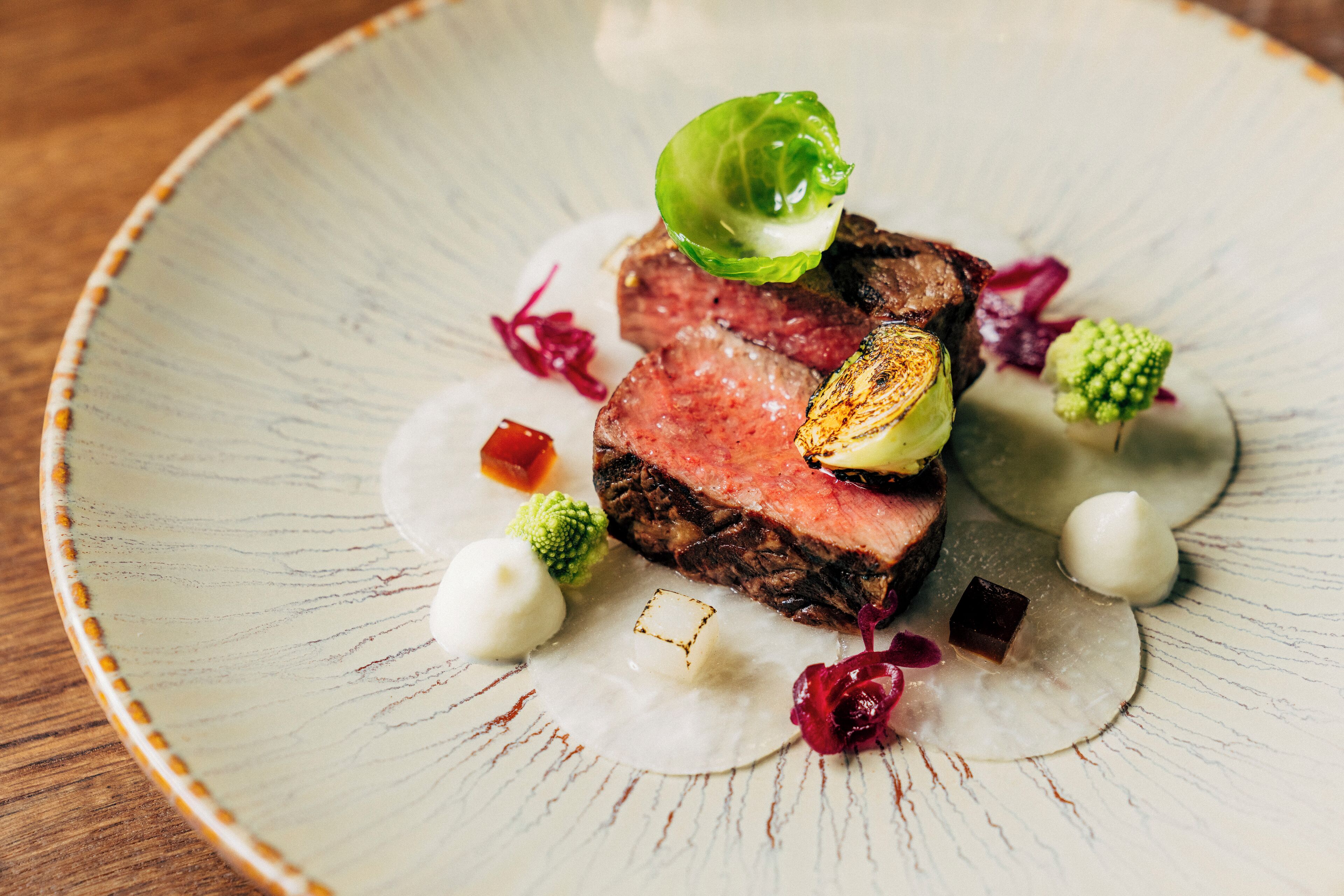A plate of food with a piece of meat, vegetables, and a decorative leaf.