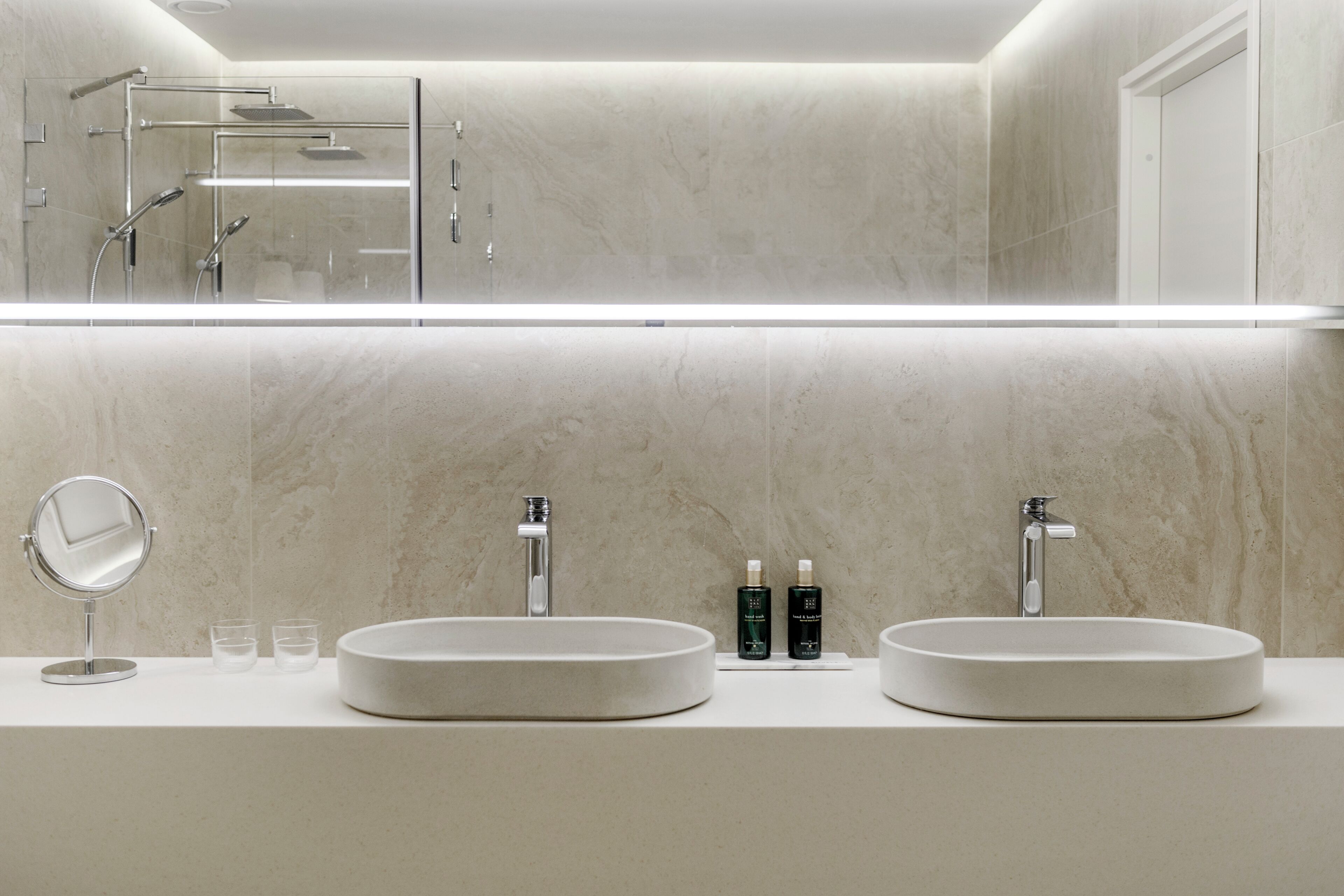 Un baño moderno con dos lavamanos, un espejo y zona de ducha.