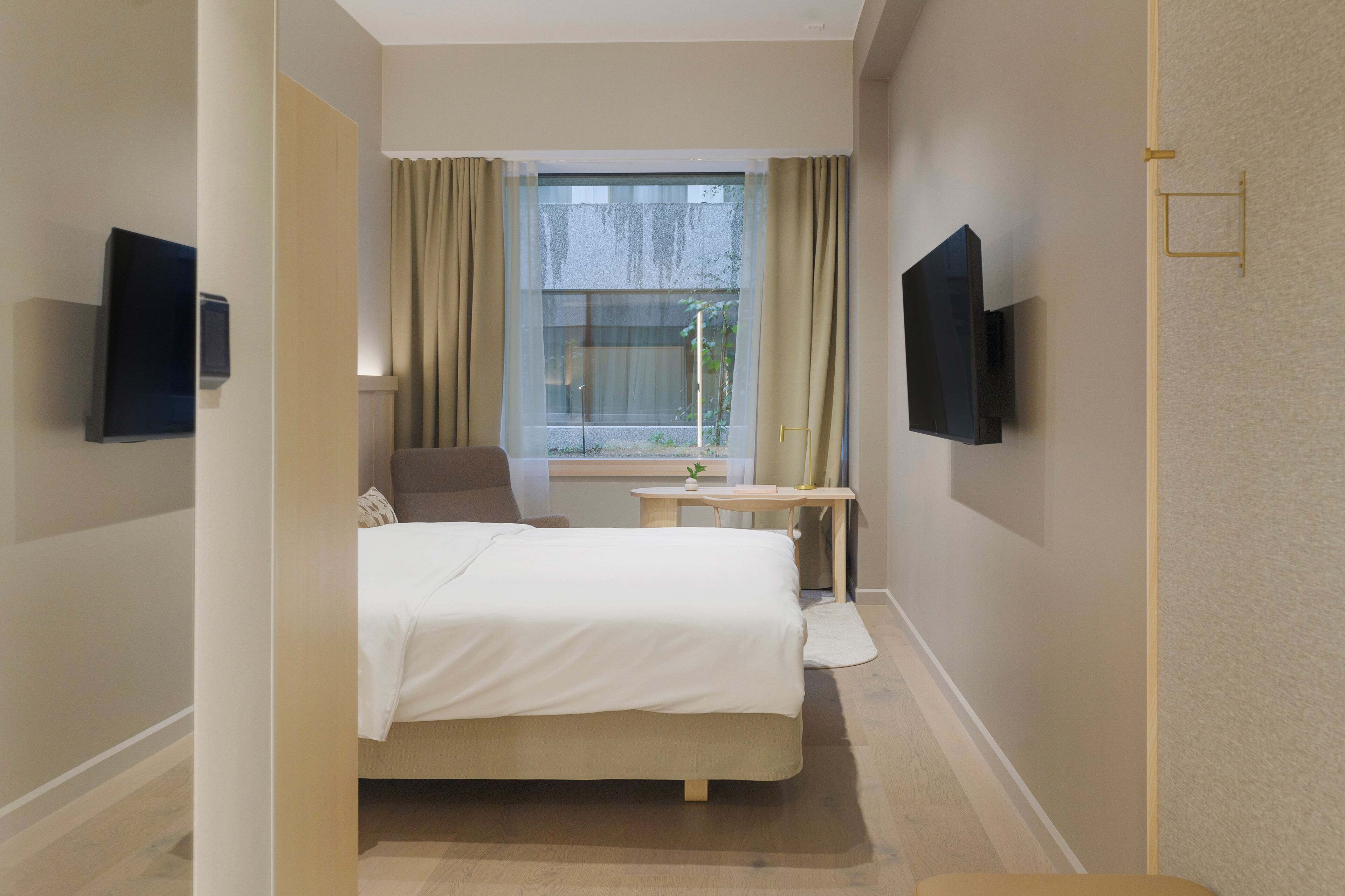 Una habitación de hotel con cama, escritorio, silla, televisor y ventana con cortinas.
