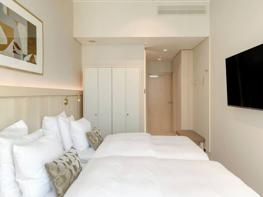 Ein Hotelzimmer mit einem großen Bett, einem Flachbildfernseher, einem gerahmten Kunstwerk an der Wand und einer Tür zu einem Badezimmer.