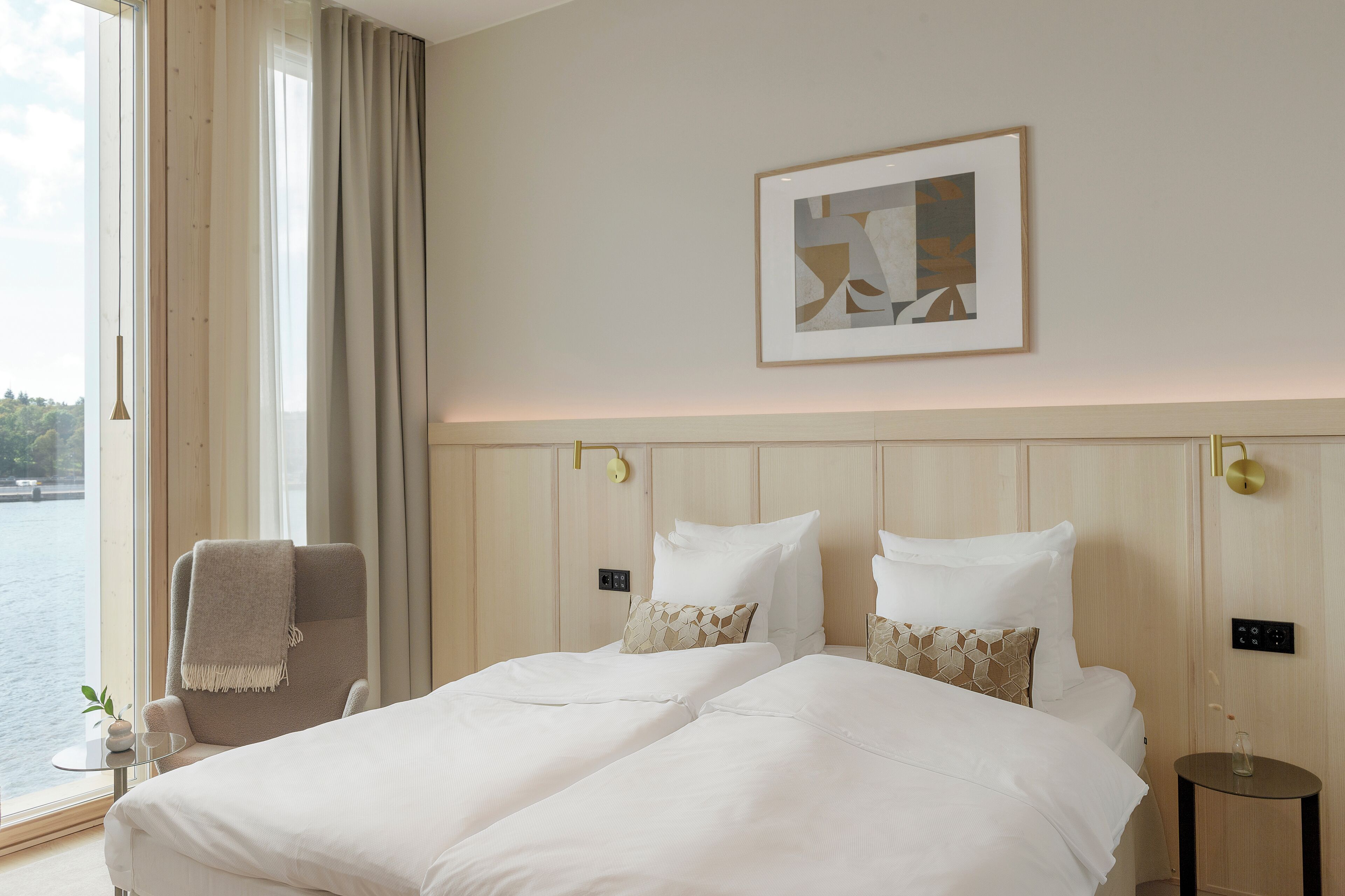 Une chambre d’hôtel avec un grand lit, une chaise avec une serviette, une petite table et une vue sur une étendue d’eau.