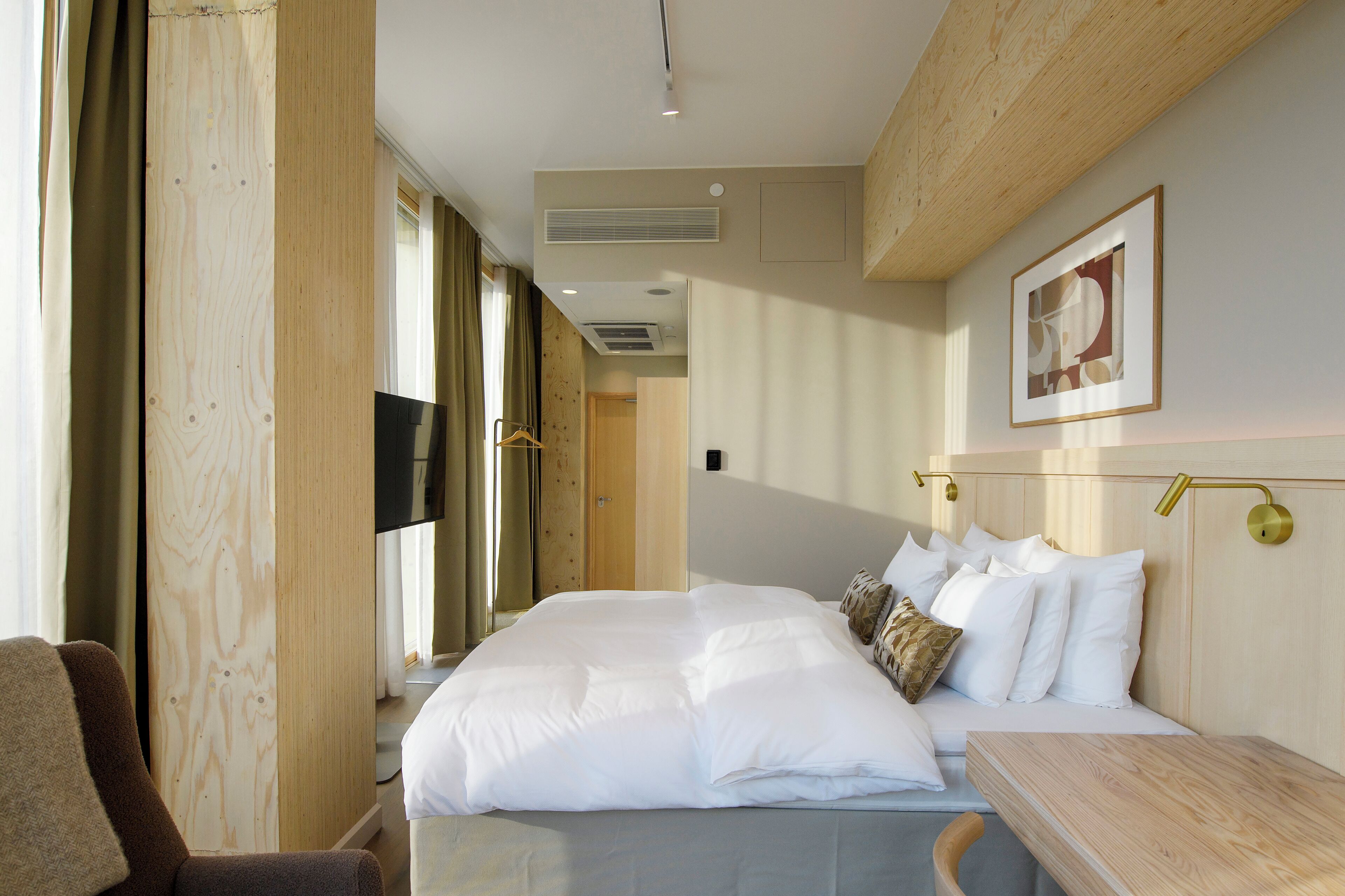 A hotel room with a large bed, a wooden headboard, a bedside table, a chair, and a painting on the wall.