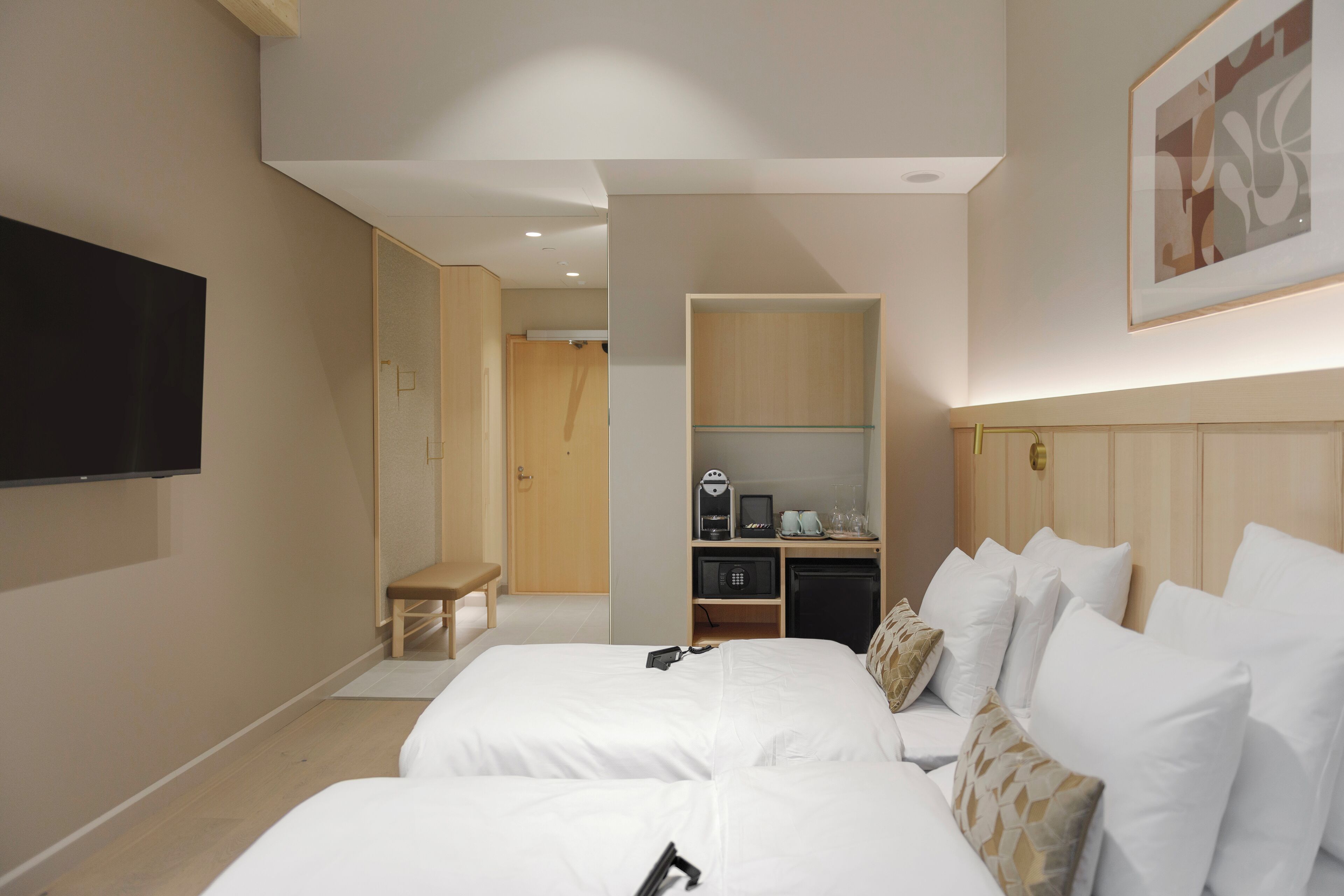 A hotel room with two beds, a desk, a television, and a kitchenette.