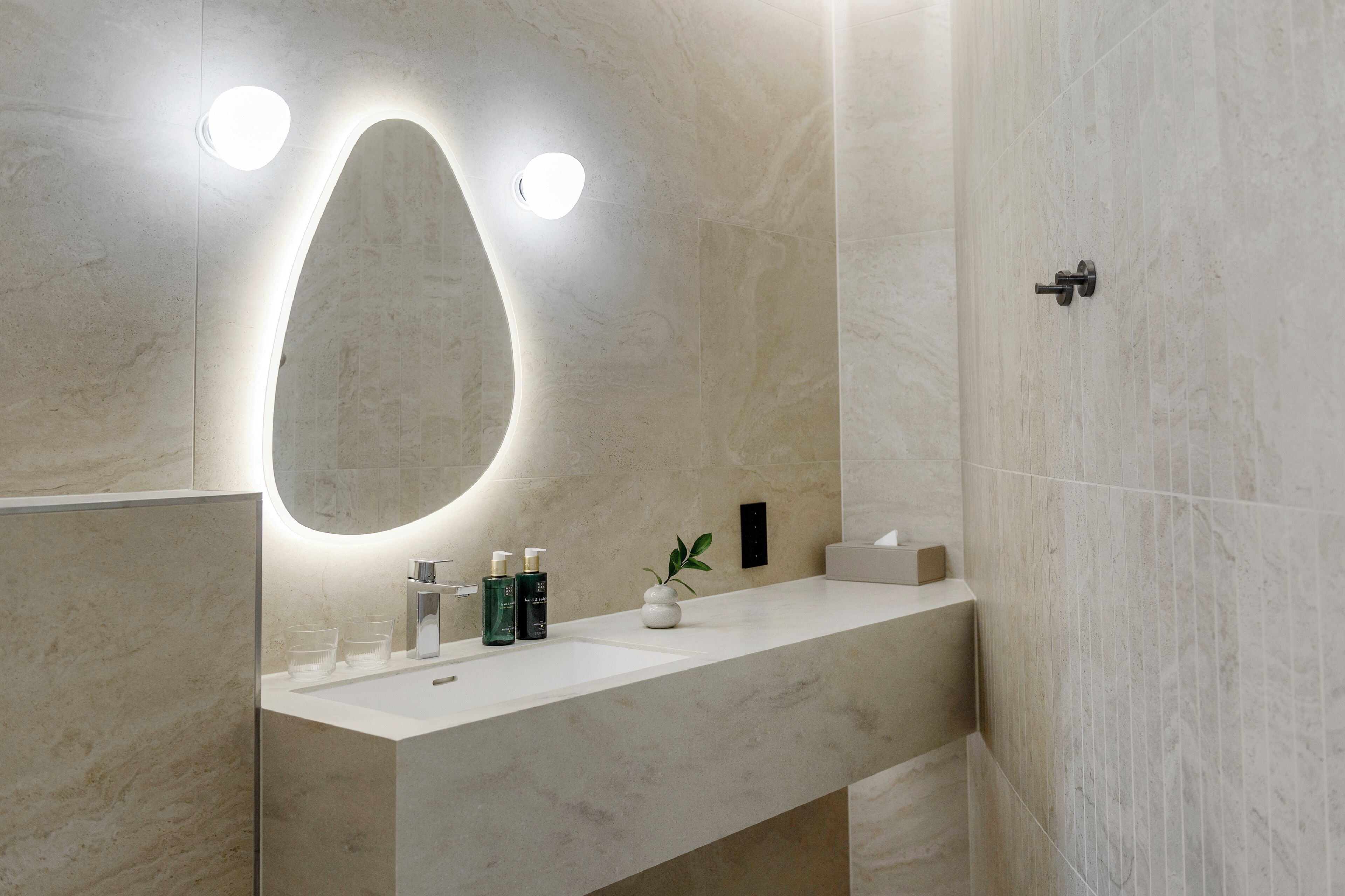 A modern bathroom with a large mirror, a white sink, and a small plant.