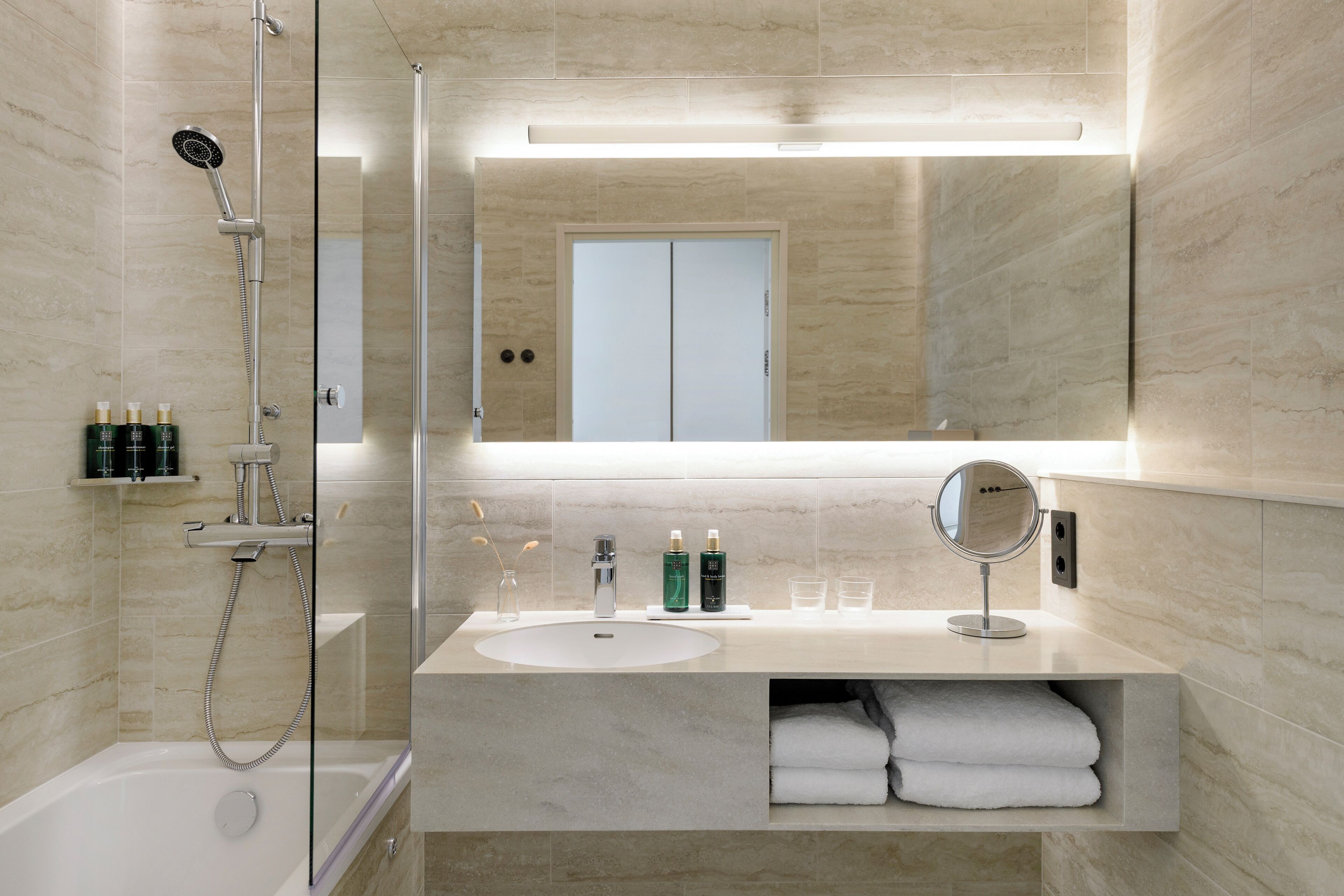 Un bany modern amb dutxa de vidre, un lavabo amb mirall i tovalloles arremegades amb cura.
