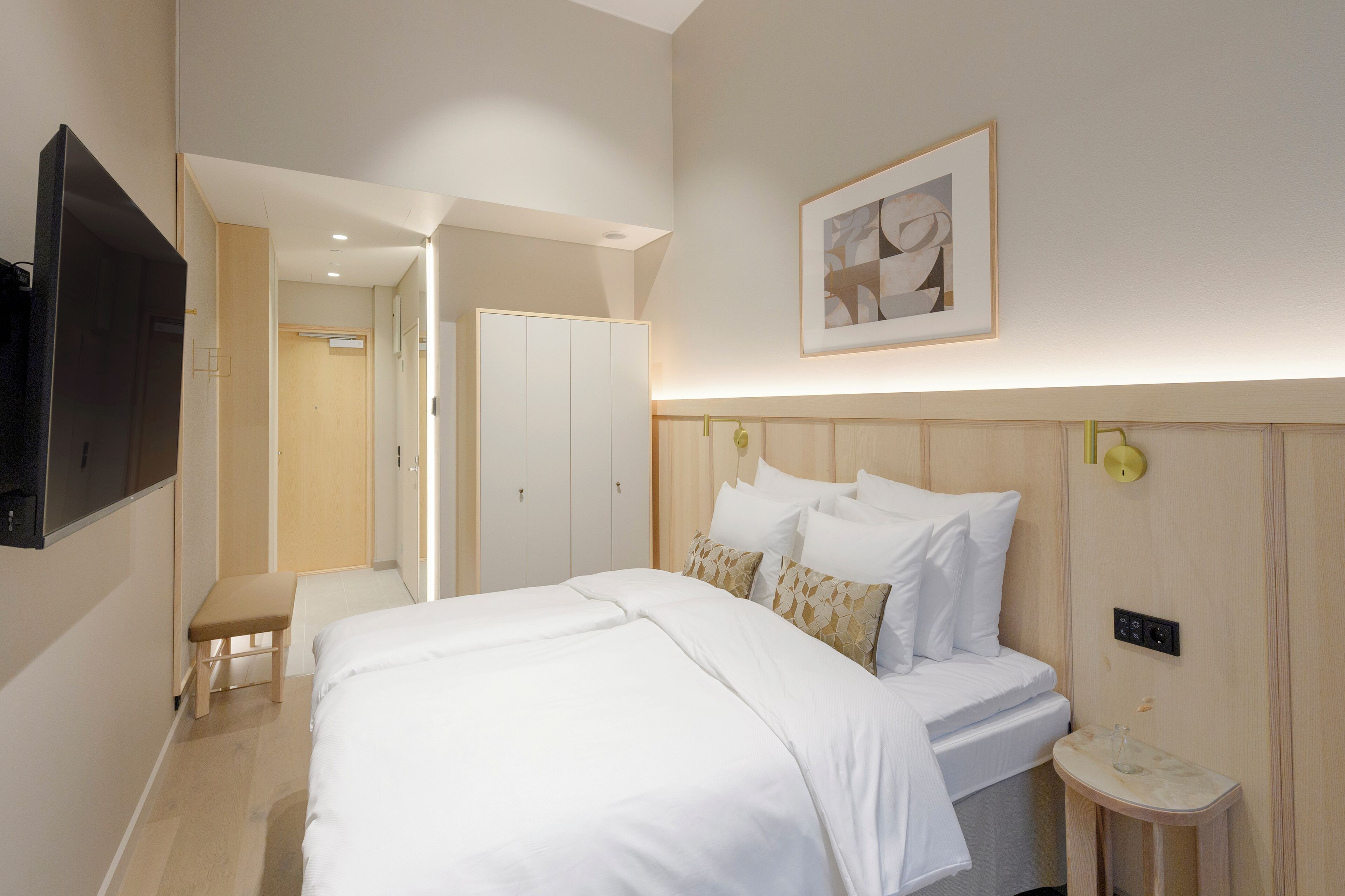 A hotel room with a bed, bedside table, and a TV mounted on the wall.