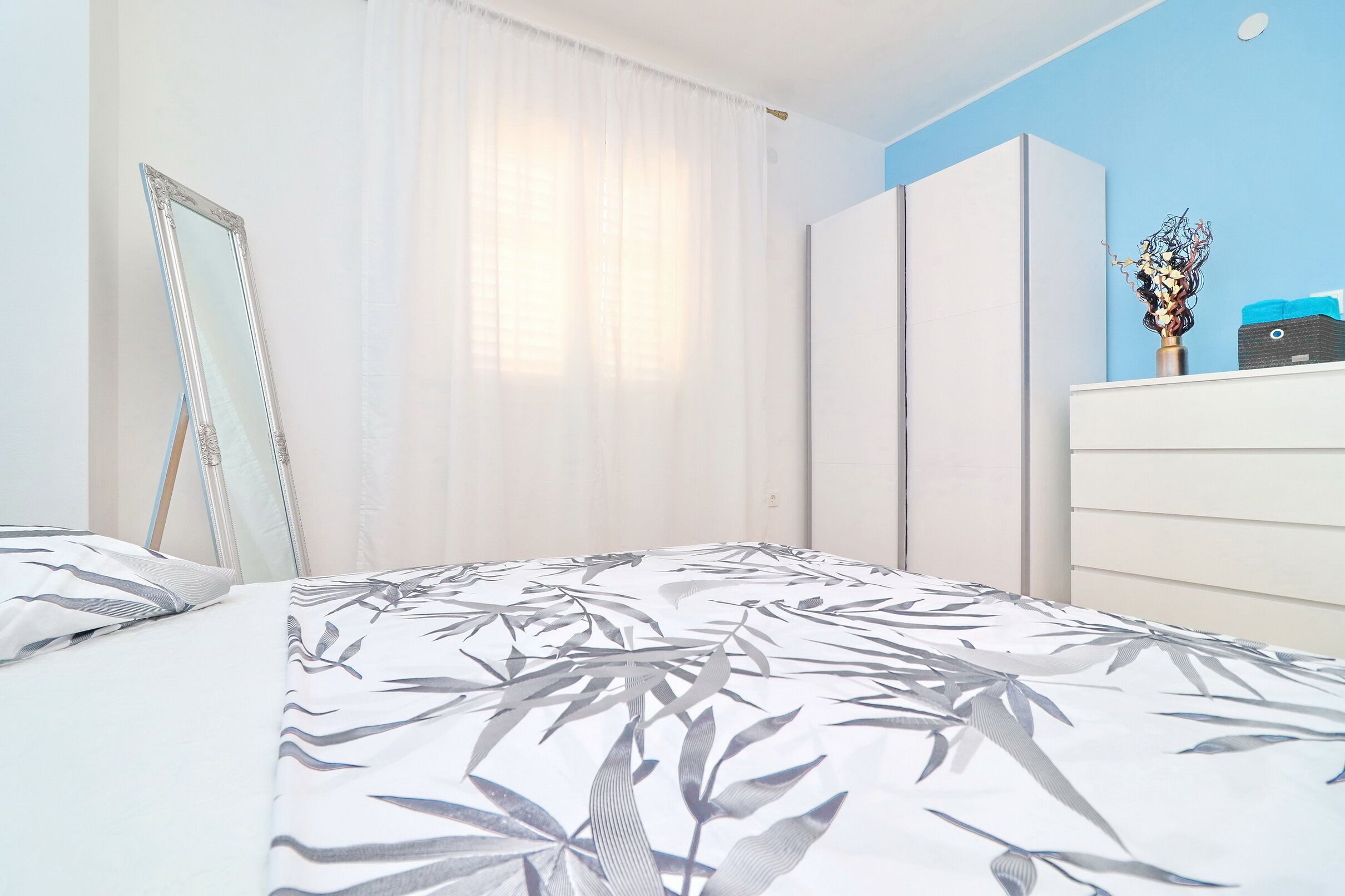 Un dormitorio con cama, armario, espejo y cómoda.