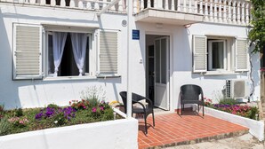 A building with white exterior walls, a balcony with white balustrades, and a sign indicating a restaurant. There are two chairs outside on a tiled patio. - Apartment Semi (Dubrovnik)