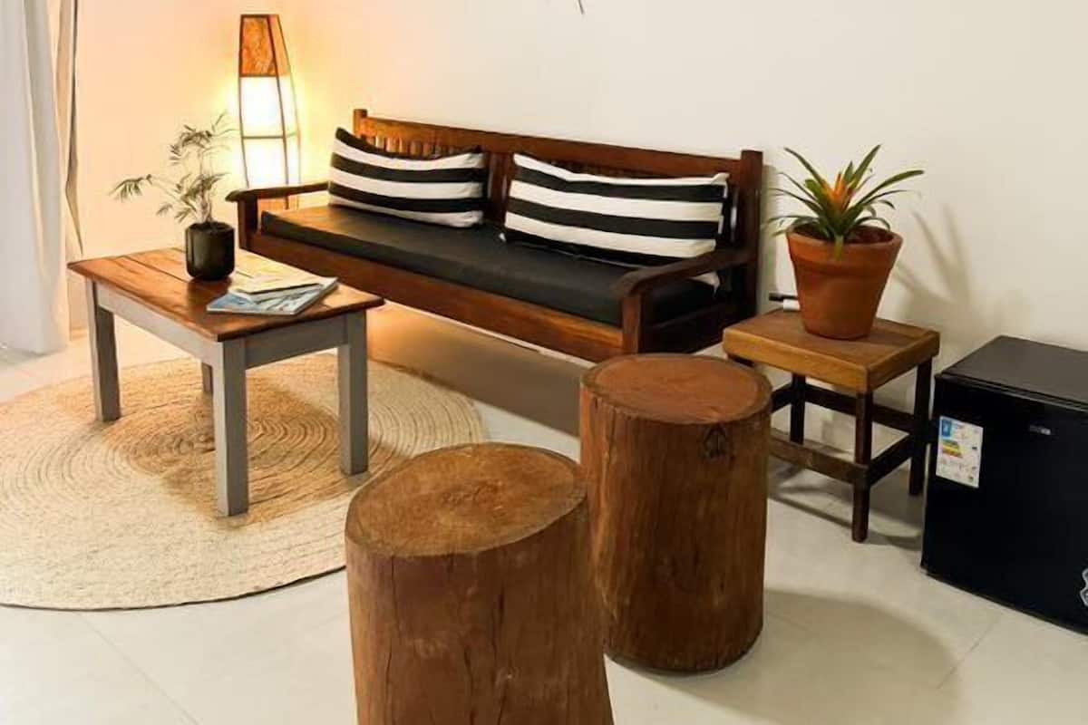 Una sala de estar acogedora con techo de madera, un sofá con cojines a rayas, una mesita de centro, una lámpara, una planta en maceta y un electrodoméstico negro pequeño.