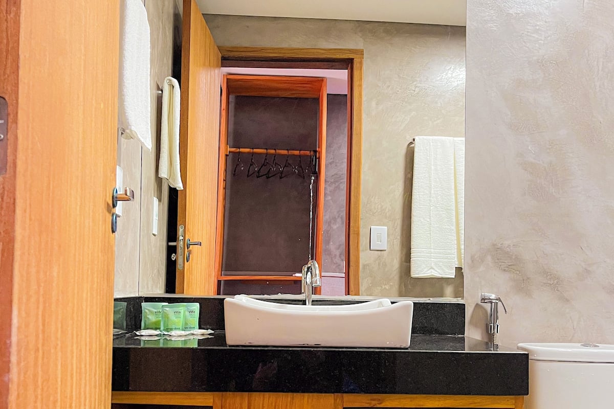 Un baño con tocador de madera, un lavabo y un inodoro. Hay cestas en el tocador y una toalla colgada en la pared.