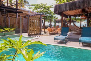 A poolside area with lounge chairs, a table, and a thatched-roof structure.