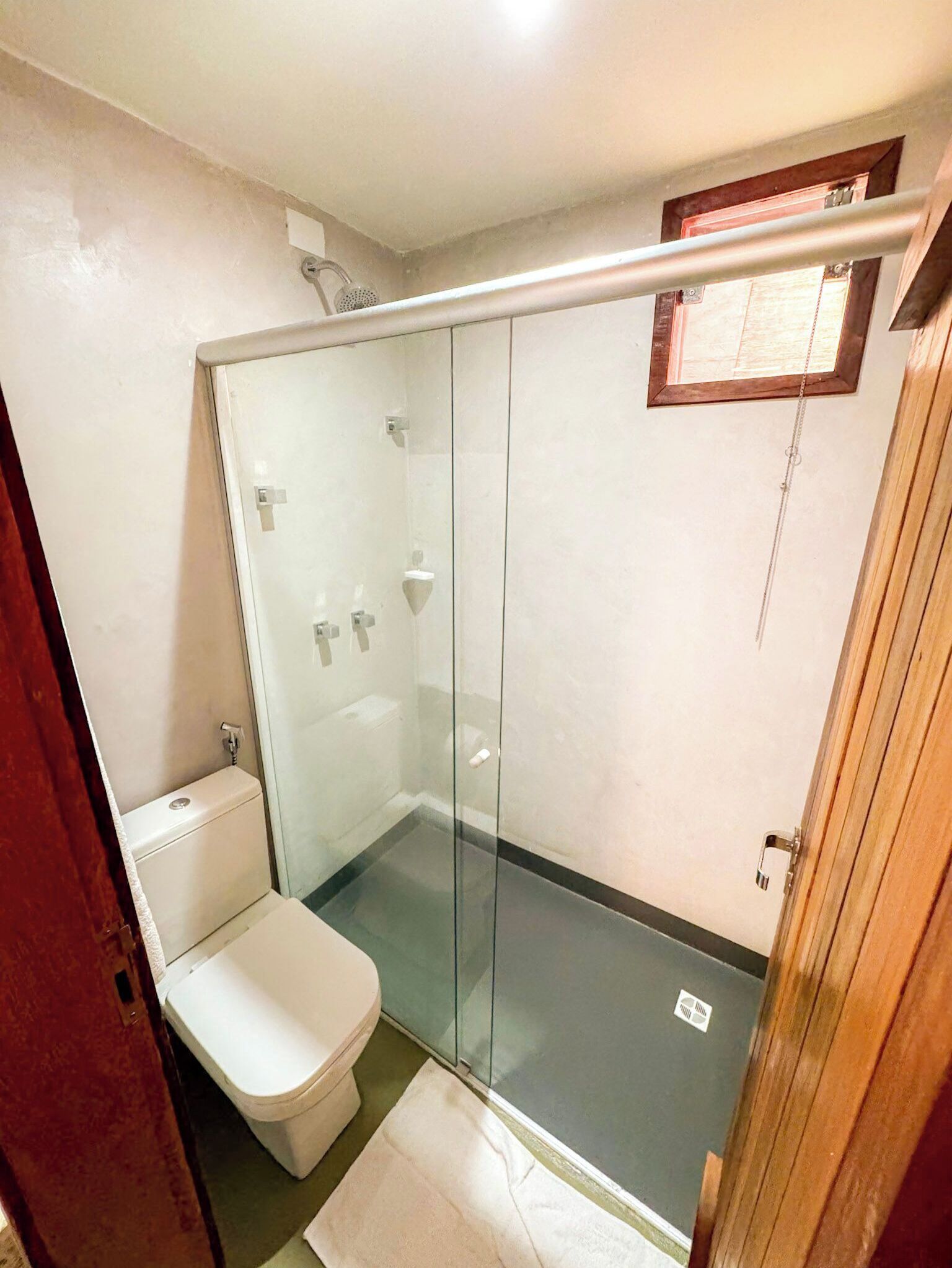 A small, enclosed shower area with a glass door, a toilet, and a wooden door frame.