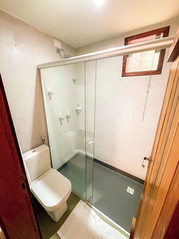 A small, enclosed shower area with a glass door, a toilet, and a wooden door frame.