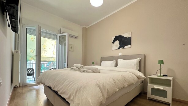 Une chambre à coucher comprenant un lit, une table de chevet, une œuvre d’art accrochée au mur et une porte ouverte donnant sur un balcon.