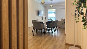 Un espace de repas moderne avec un plancher en bois, une table ronde et quatre chaises. Un téléviseur est fixé au mur et une fenêtre offre une vue sur l’extérieur.