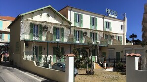 A hotel with a white facade, green shutters, and a balcony. - Hôtel L'ÎLOT FLEURI  (Le Lavandou)