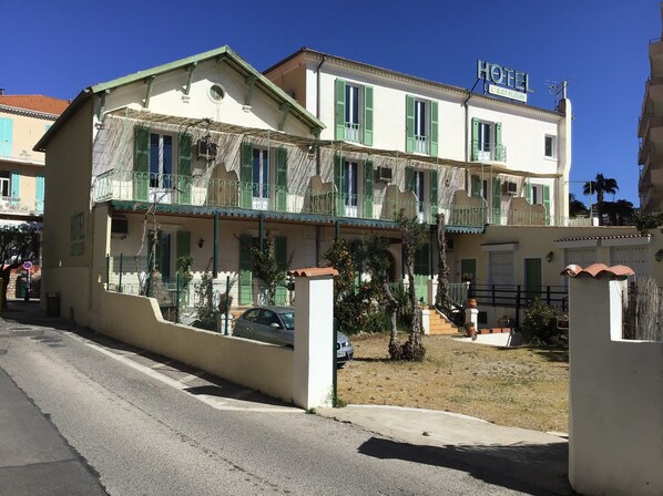 Un hotel con fachada blanca, contraventanas verdes y un balcón.