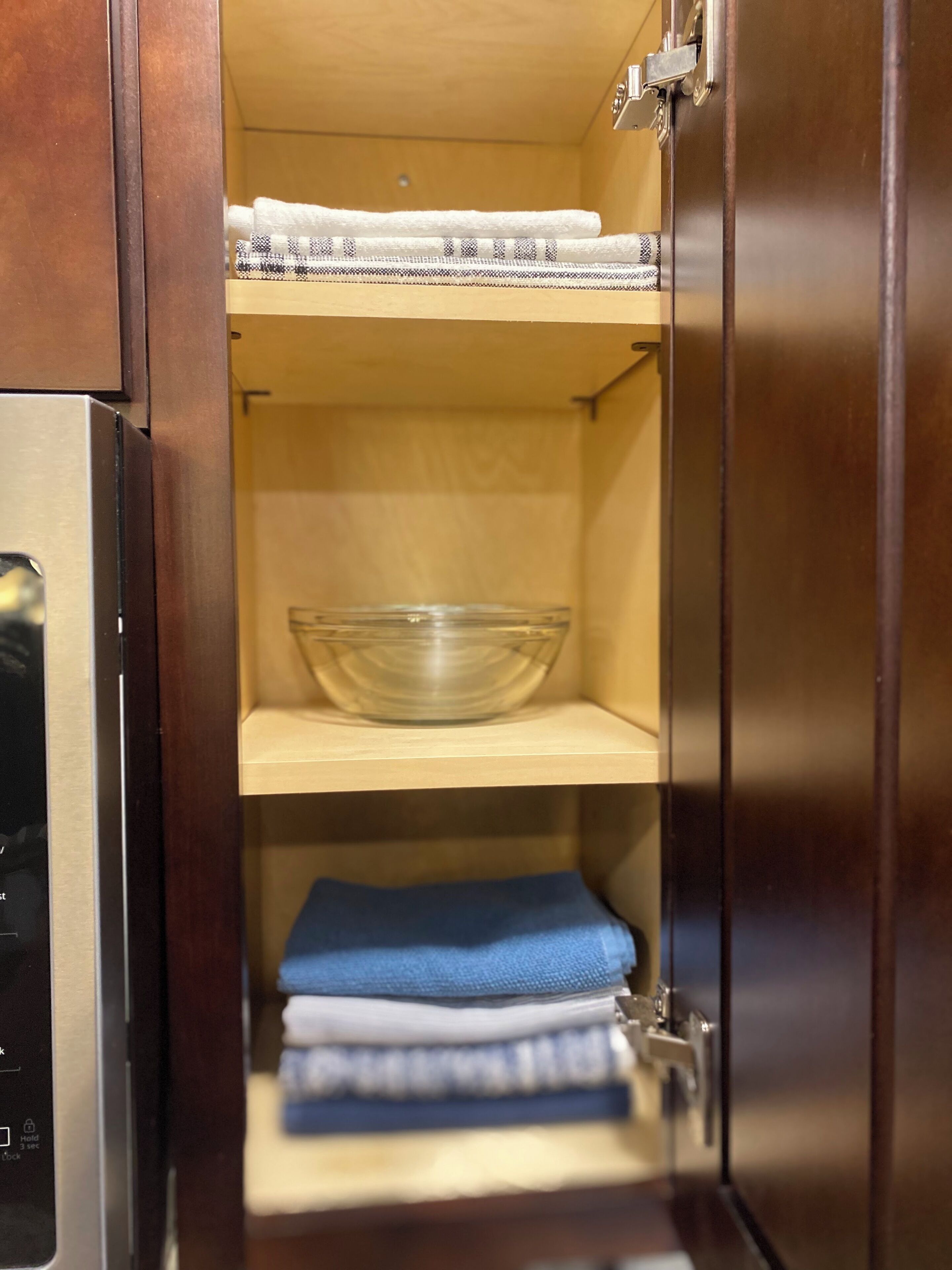 A kitchen cabinet with a microwave, a glass bowl, and folded towels.