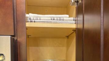 A kitchen cabinet with a microwave, a glass bowl, and folded towels.