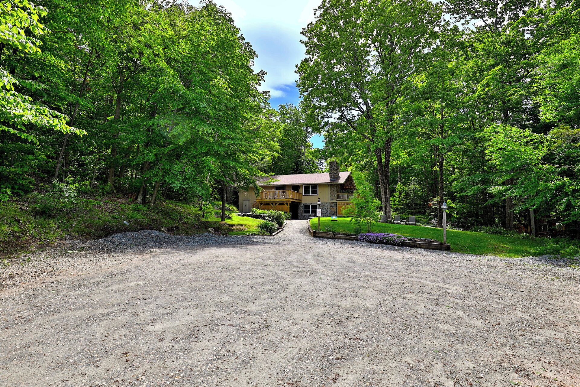 A rustic lodge with a gravel driveway leading to a wooden deck and a stone building.